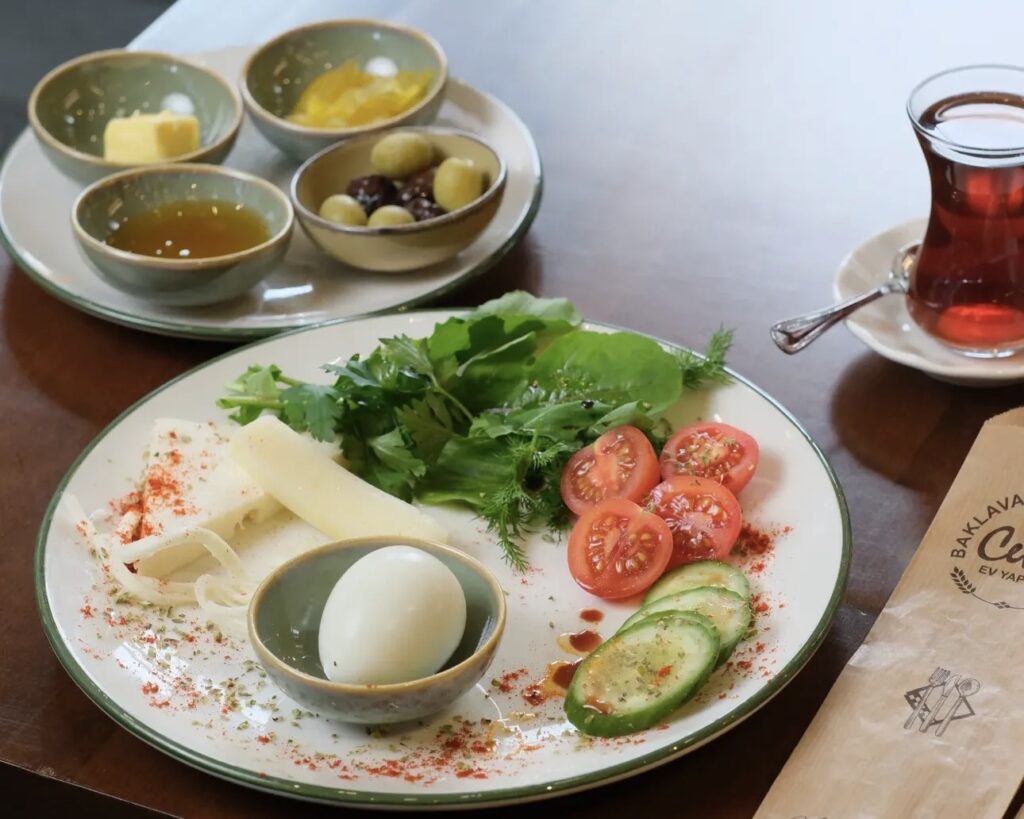A single-serving traditional breakfast plate at Ceviz Ev Yapımı with a boiled egg, feta cheese, olives, honey, butter, and fresh vegetables.